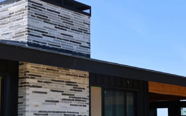 Custom home exterior under construction with stone veneer and black trim against a clear North Texas sky